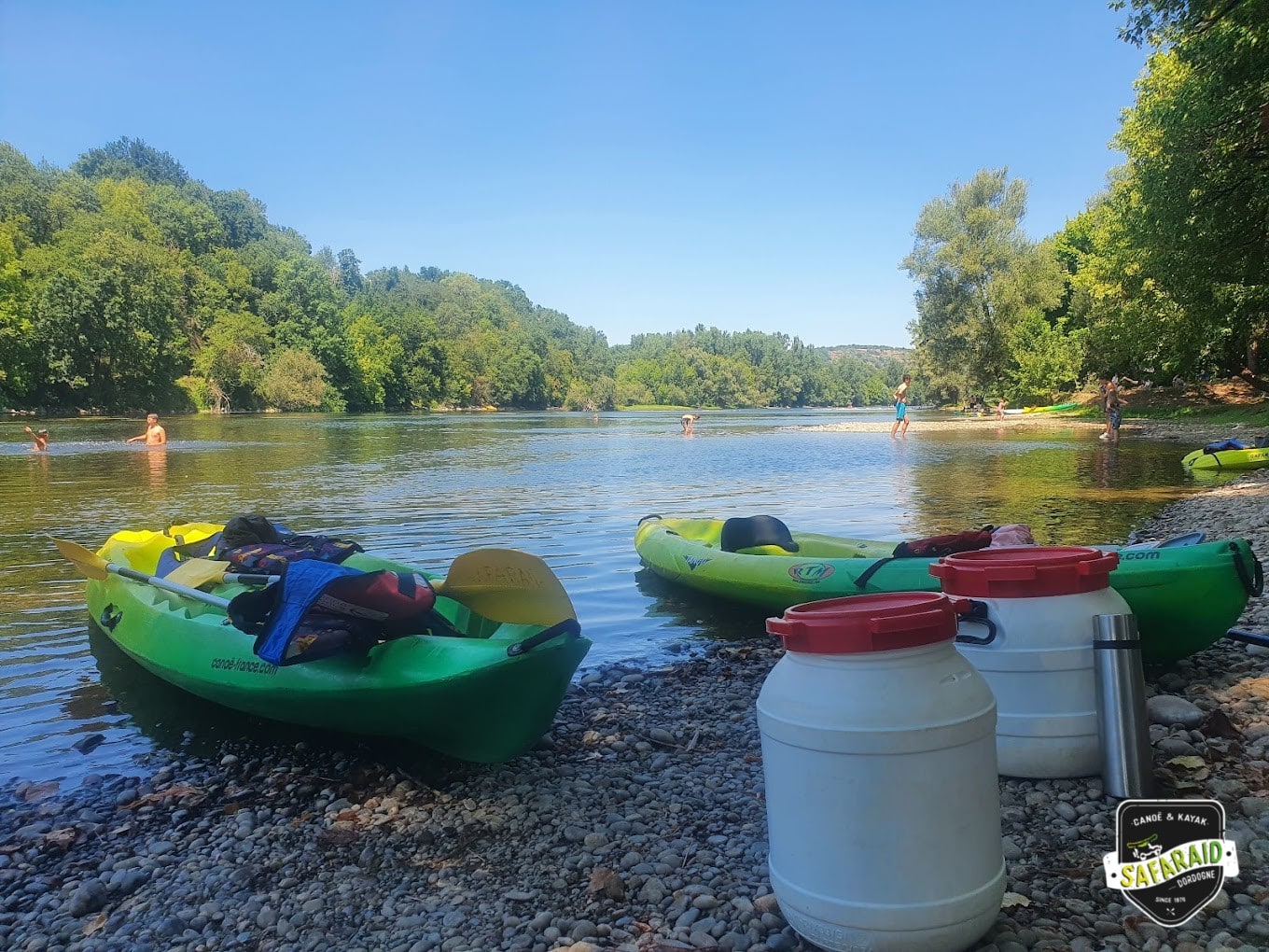 Deux kayaks au bord de l'eau sur une plage de galet ombragé.