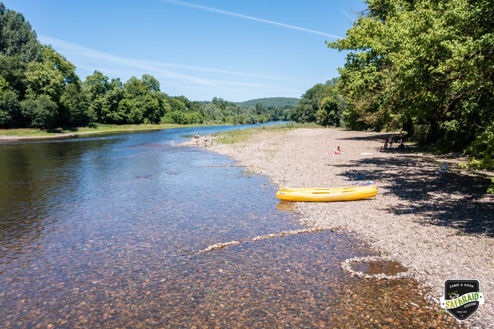 Plage de galet au milieu des arbres à coté d'une rivière avec des kayaks jaunes posés au bord.