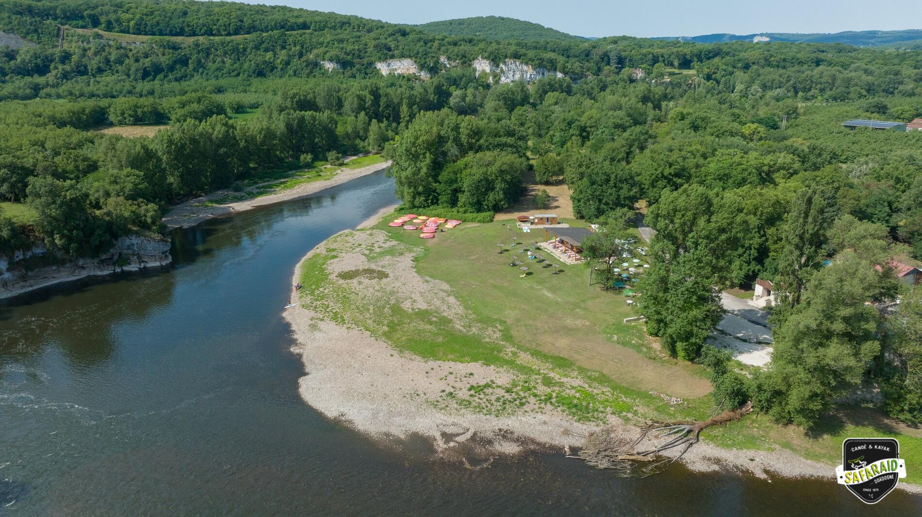 Rivière et une grande plage de galet en pleine nature au milieu des falaises avec juste à côté une guinguette, vue du ciel.